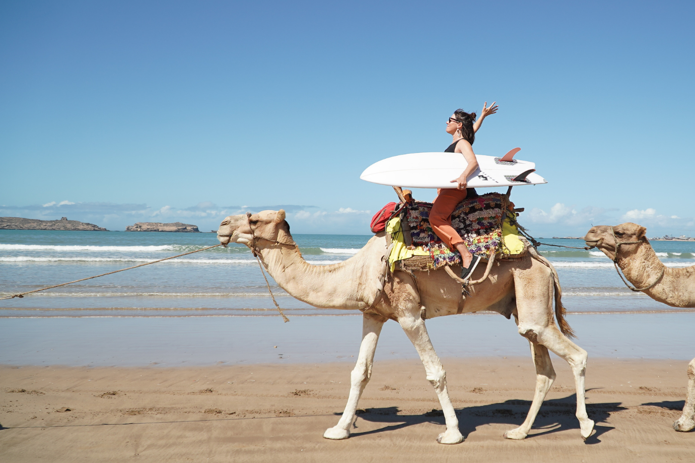 A lady on a camel with a surfboard enjoying her time on a Surf With Amigas Retreat