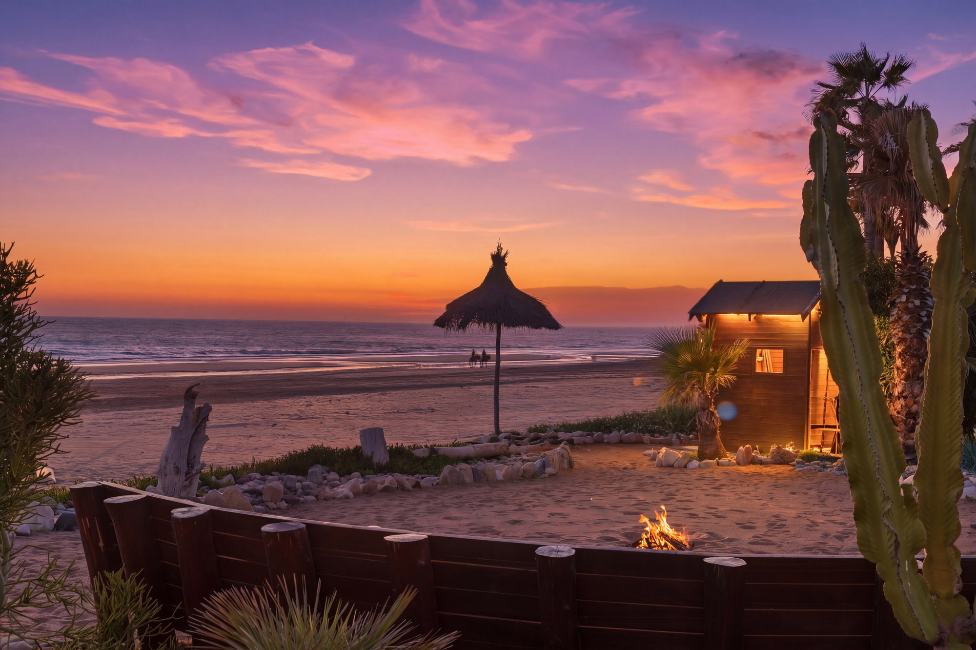 Beach fire pit and thatched parasol at sunset on the sand at Imi Ouaddar, Paradis Plage, Morocco