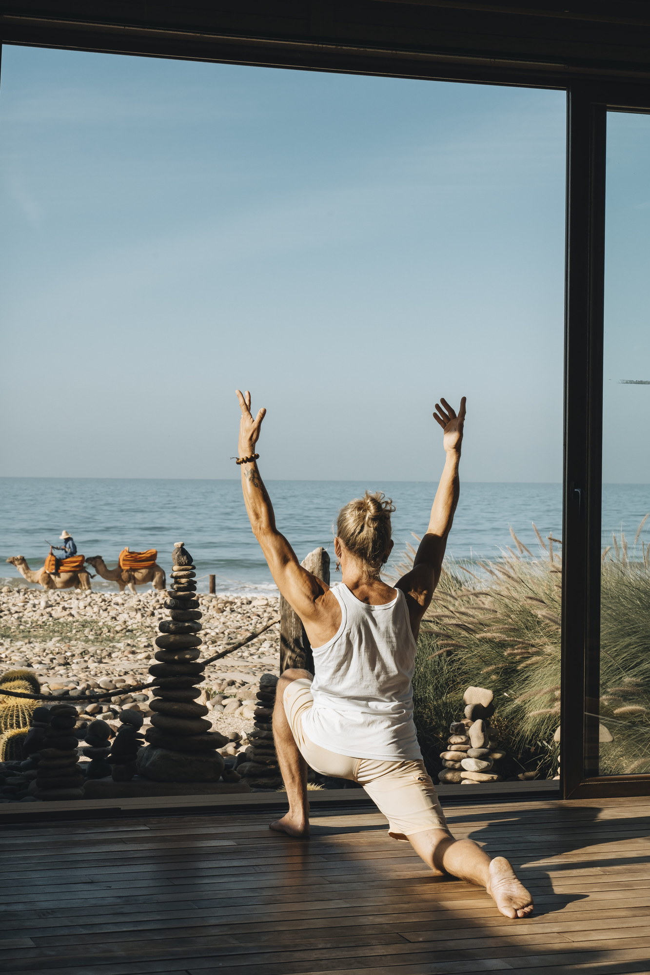 Sunrise yoga in the glass-walled oceanfront shala at Paradis Plage, with camels passing along the beach outside