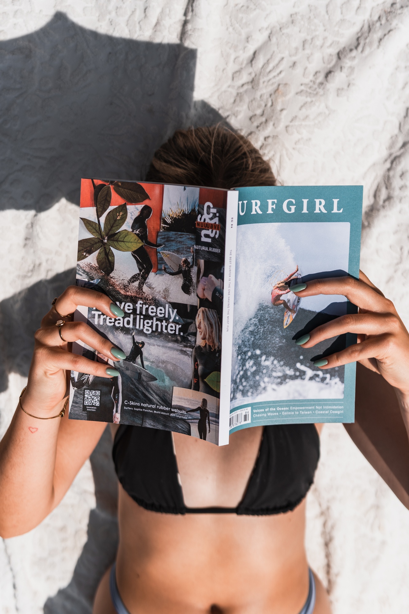 A reader sitting on the beach with a copy of SurfGirl Magazine open in her hands.
