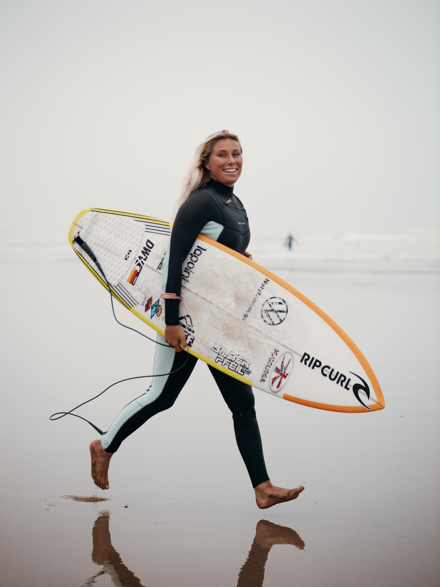 Surfer walking up the sand with a Rip Curl shortboard under one arm