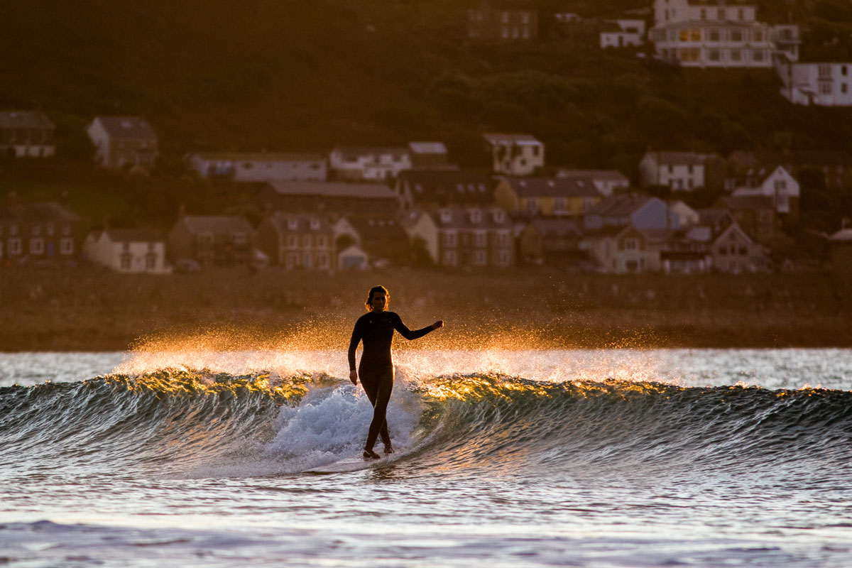 Izzy Henshall surfing a glassy wave at sunset in Cornwall