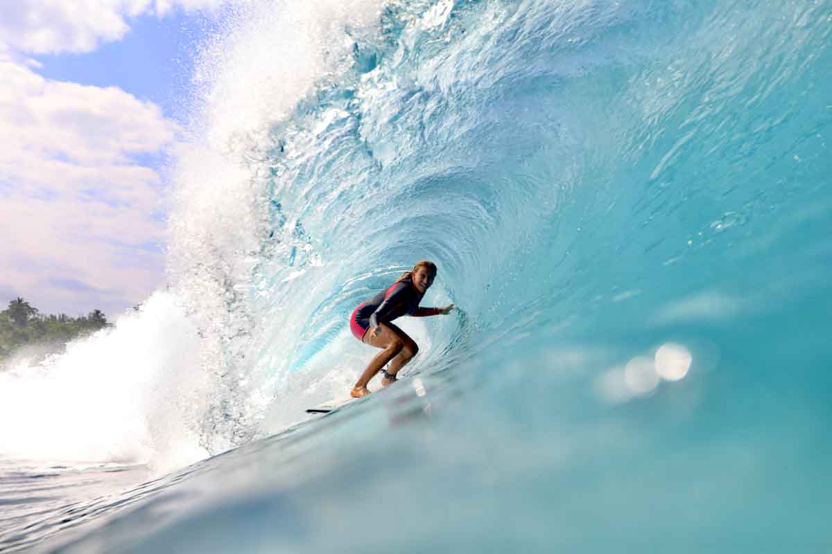 Jaleesa Vincent stands tall inside a clear blue barrel in a red and black springsuit, looking back towards the camera