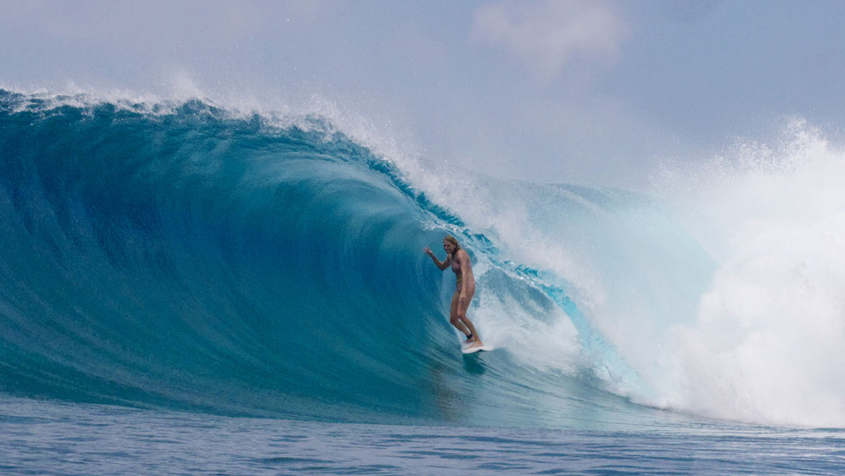 A surfer stands tall inside a deep blue barrel