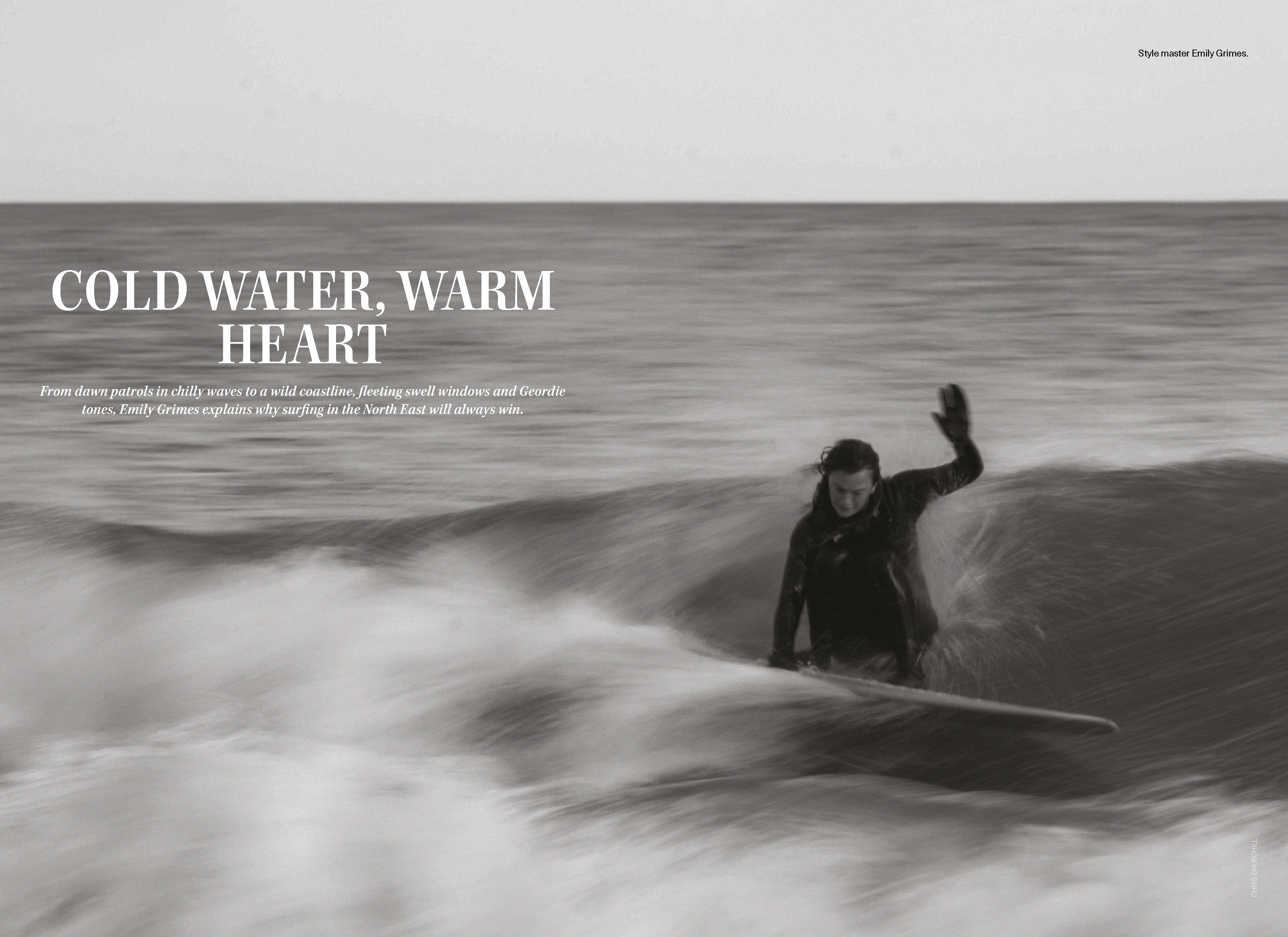 Black and white magazine spread of Emily Grimes in a hooded wetsuit riding a longboard through grey North East England surf, with the headline Cold Water, Warm Heart