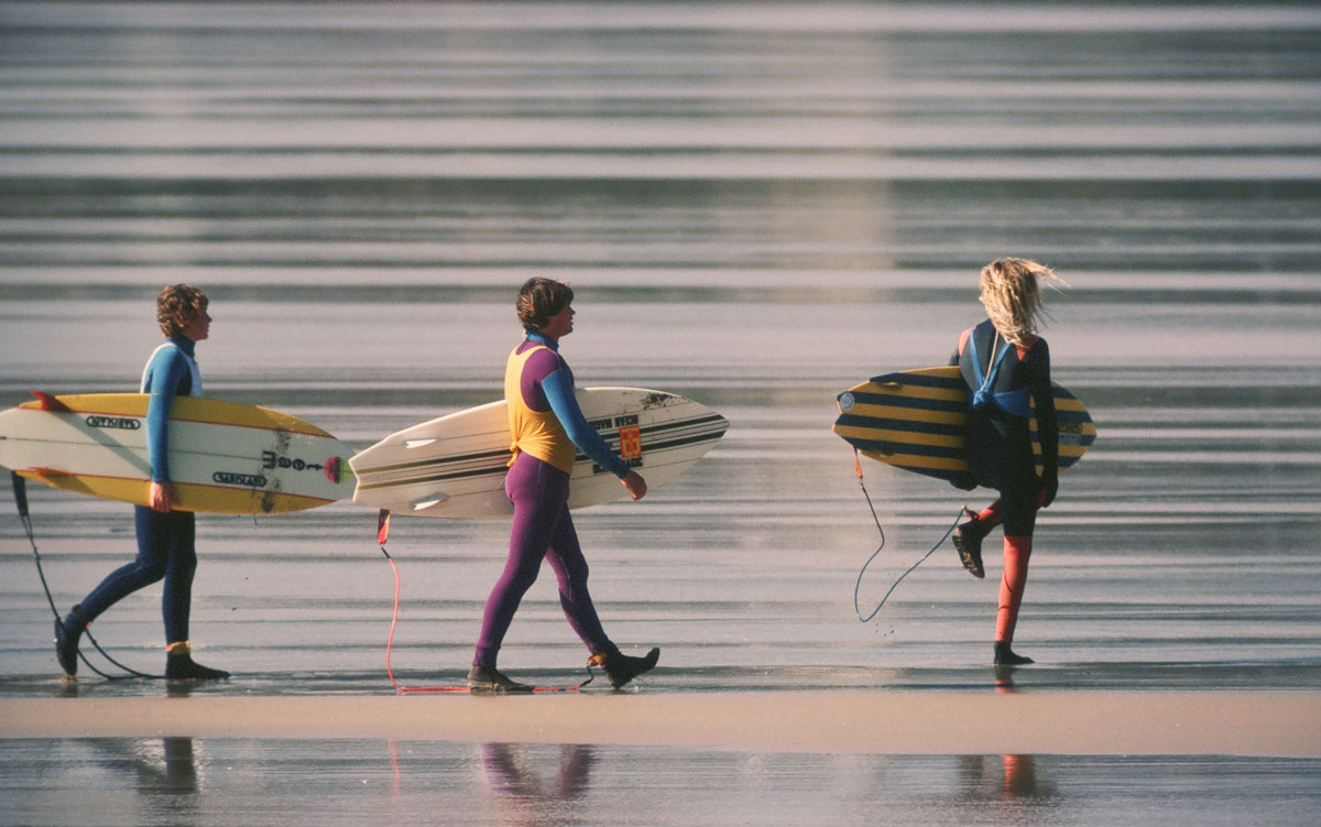 Three surfers carrying boards along the beach at the Newquay Surf Classic