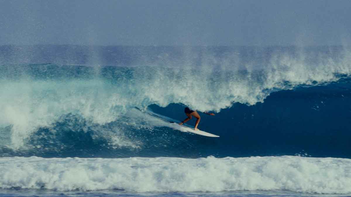 A surfer pulls into a deep blue barrel as spray blows back off the lip