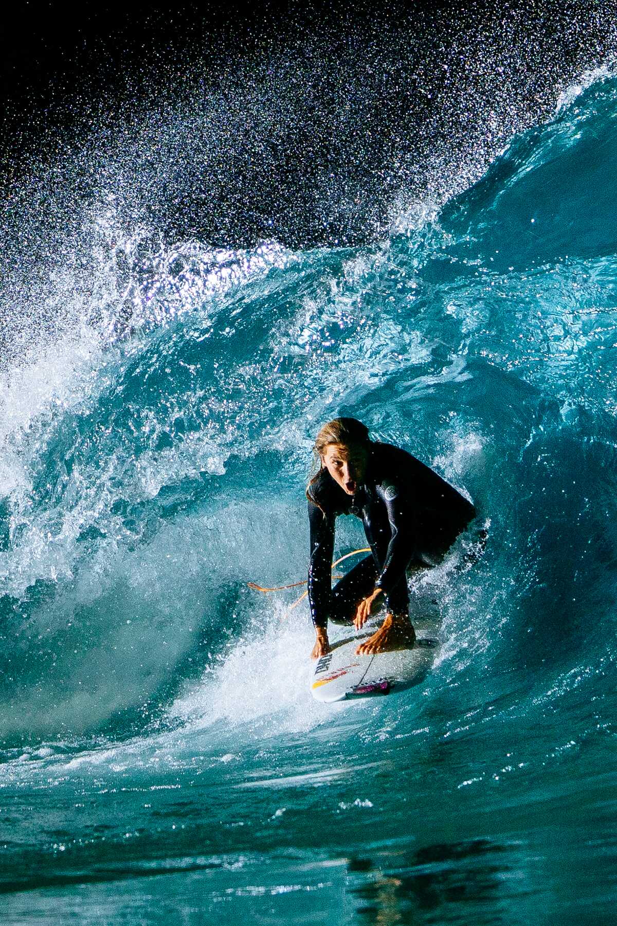 Surfer crouched in a deep blue barrel under floodlights