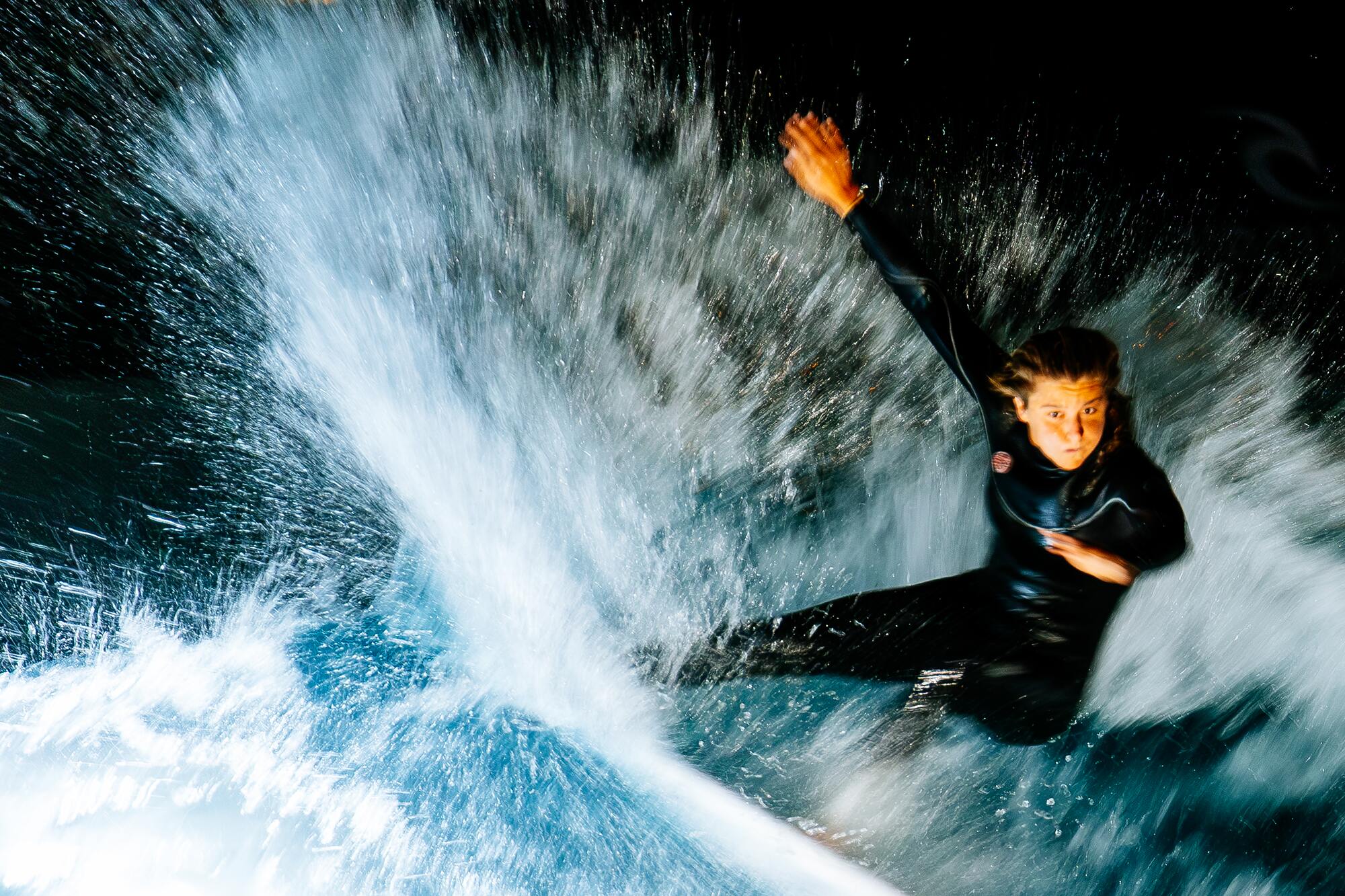 Surfer throwing spray off the lip of a floodlit wave at night
